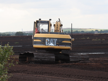 A digger sat in a peatland that has been stripped bare of life to make commercial compost