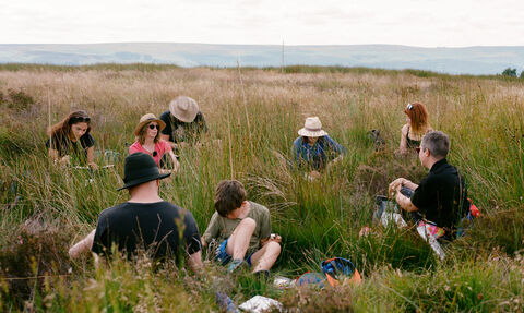 A group people sitting on a peatland, sketching the landscape around them