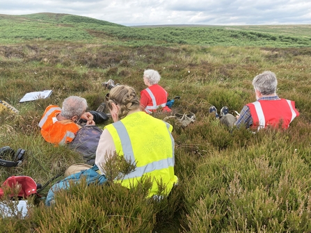 A group of people sat on moorland writing poetry