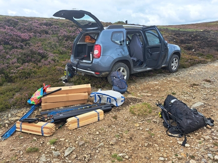 A vehicle parked on an off-road track; next to it on the track are packs of wooden stakes and boxes of monitoring equipment.
