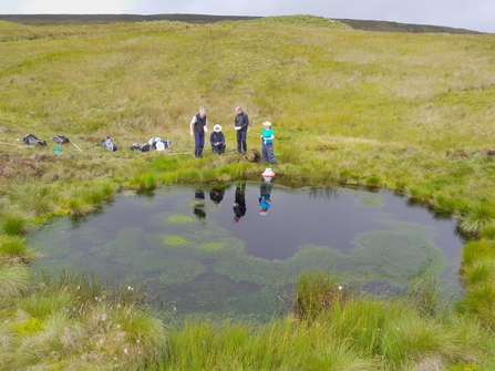 A group of people stood at the edge of a bog pool on open moorland
