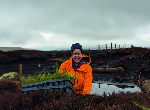 Volunteer smiling to camera as she plants crowberry plugs