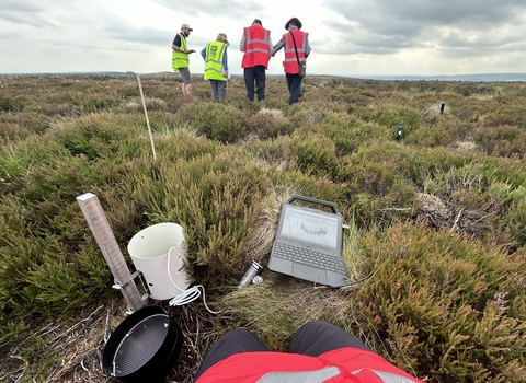 Four people in hi-vis collecting rain gauge data on a moor