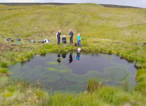 A group of people stood at the edge of a bog pool on open moorland